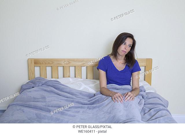 Young woman sitting on her bed, covered by a blanket