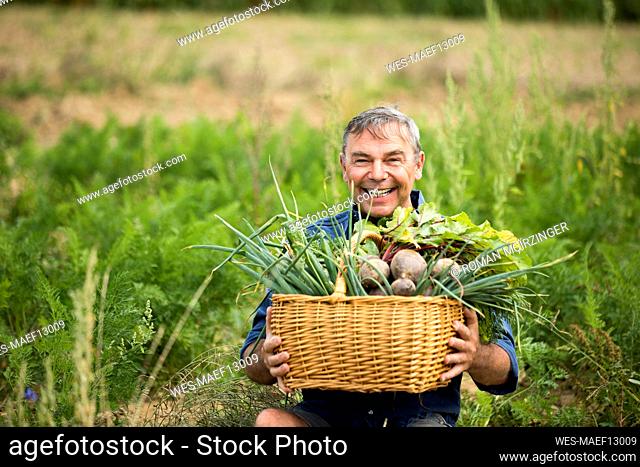 Man holding vegetable basket while sitting at farm