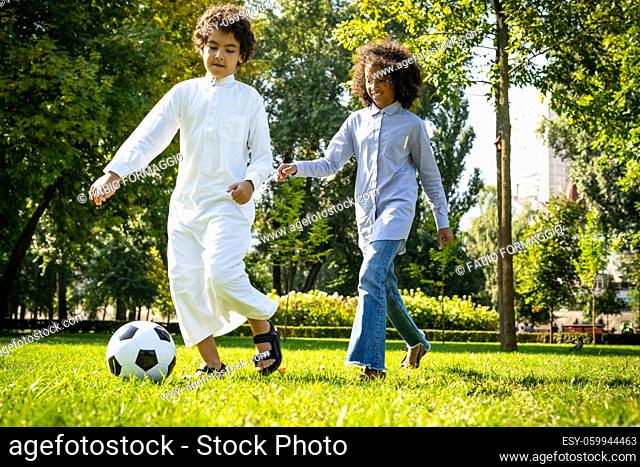 cinematic image of a family from the emirates spending time at the park. Brother and sister playing soccer in the grass