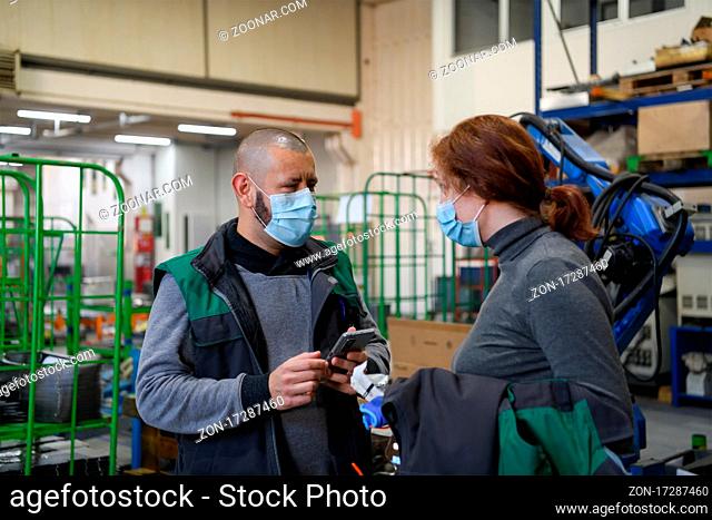 Industrial workers with face masks protected against coronavirus discussing production in the factory. People working during COVID-19 pandemic