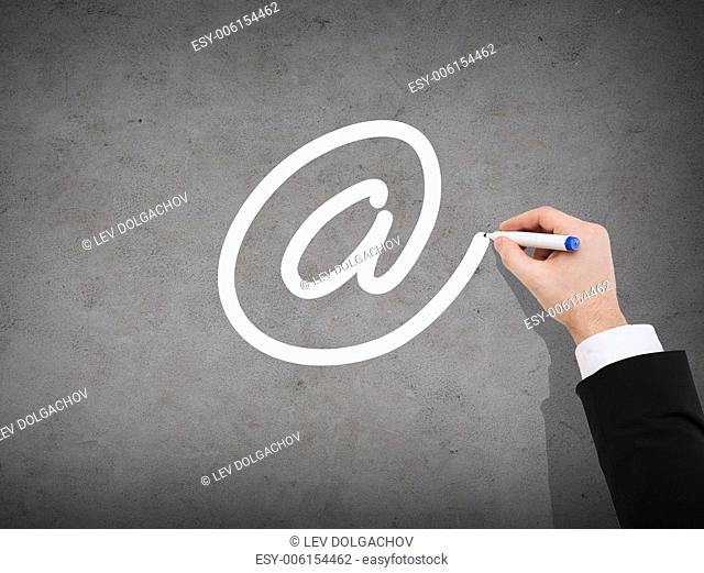 business, communication and internet concept - close up of businessman drawing e-mail sign on concrete wall