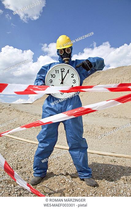 Germany, Bavaria, Man in protective wear with clock near sand dune and cordon tape in foreground