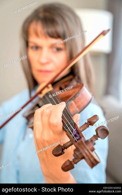 Mature woman playing violin. Focus on fingers