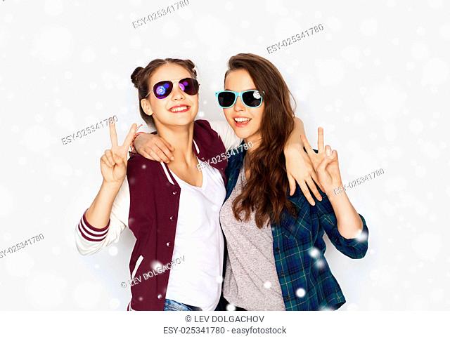 winter, christmas, people, fashion and gesture concept - happy smiling pretty teenage girls or friends in sunglasses showing peace hand sign over gray...
