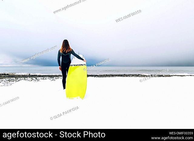 Man with surfboard standing on snow covered beach