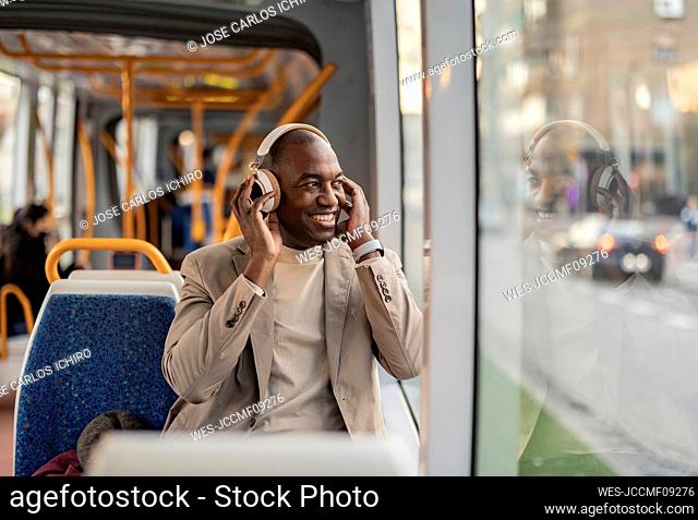 Happy commuter wearing wireless headphones and looking out of window in tram