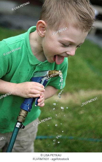 Little boy drinking from a garden hose