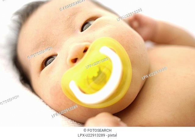 Baby with pacifier lying on bed, close up