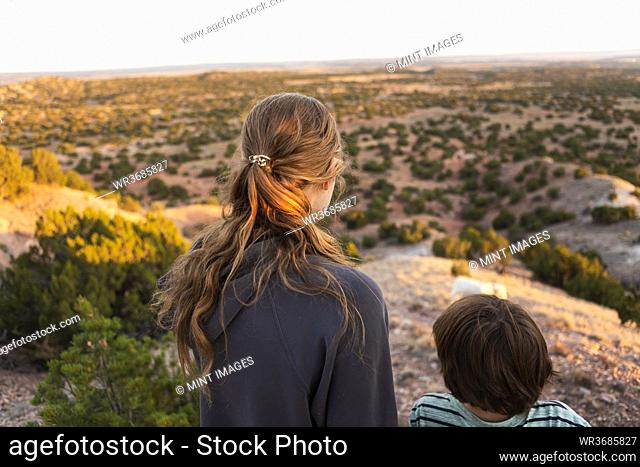 teenage girland her brother looking down at Galisteo Basin, Santa Fe, NM at sunset