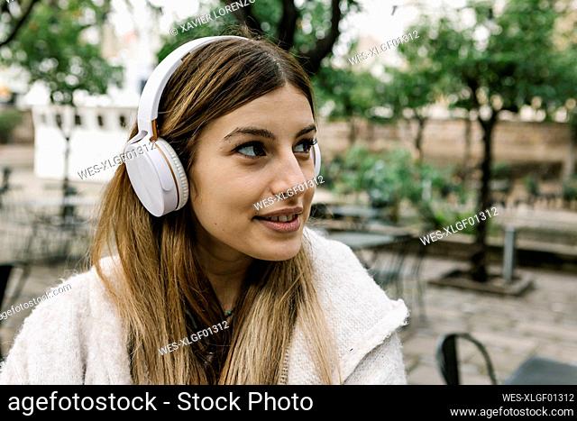 Woman with headphones looking away while smiling outdoors