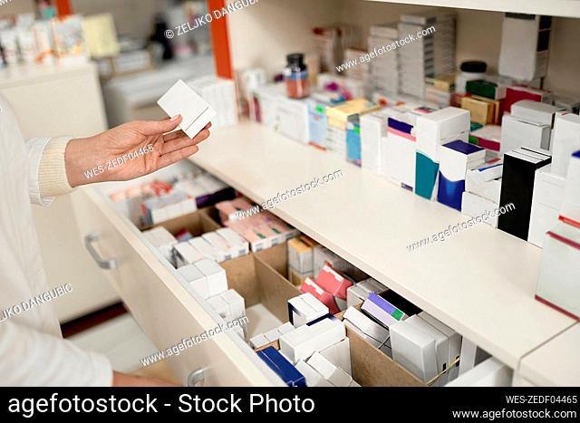 Pharmacist holding box of medicine by drawer at pharmacy store