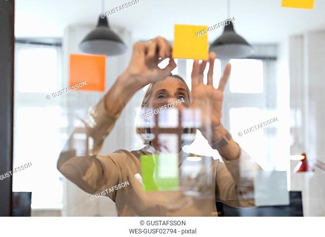 Mature businesswoman with adhesive notes on glass pane in office