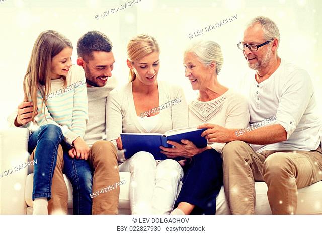 family, happiness, generation and people concept - happy family with book or photo album sitting on couch at home