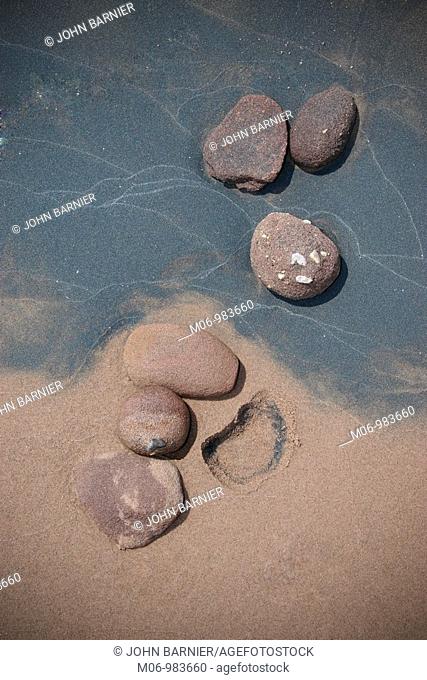 A grouping of six rocks imbedded into beach sand with the impression of one rock missing