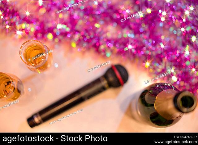 Black microphone in karaoke club, with remote controller, melon and strawberry soda drinks, yellow tambourine and screen for singing music on stage party