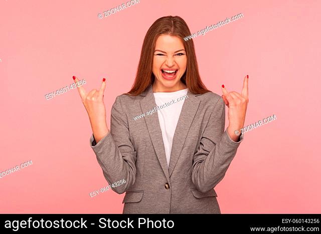 Portrait of delighted overjoyed woman in business suit showing rock and roll hand sign and yelling, looking crazy aggressive with devil horn gesture