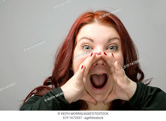 A auburn haired caucasian woman yelling shouting screaming with her hands cupped around her mouth