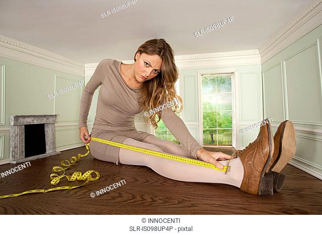 Young woman in small room measuring her leg
