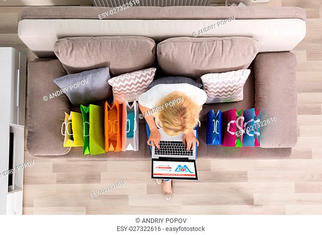 High Angle View Of A Woman Shopping Online On Laptop With Shopping Bags On Couch