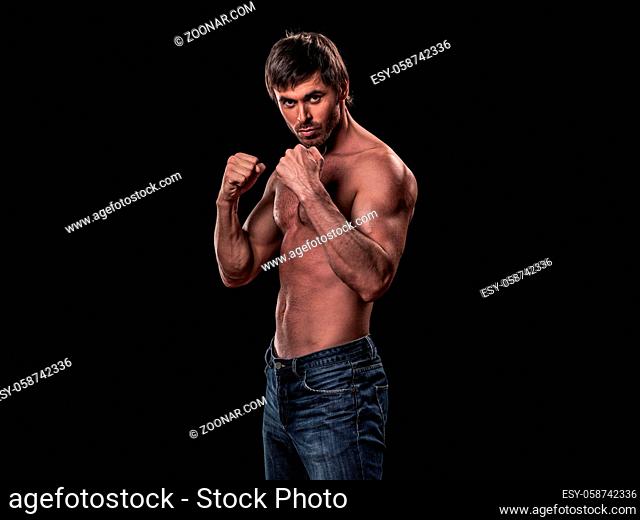 Muscular man in fighting stance holding fists ready to fight black background