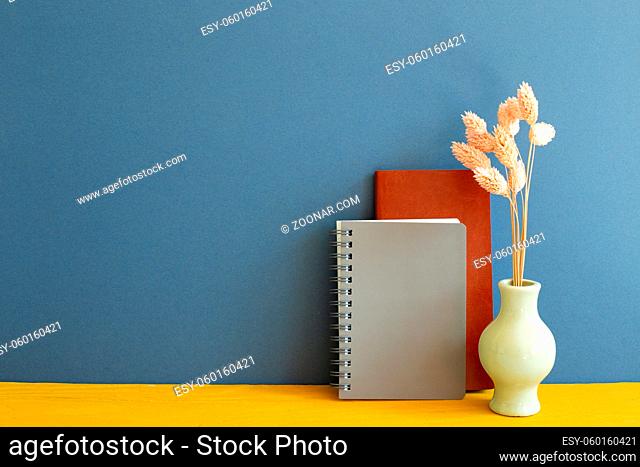 Notebook with dry flowers on yellow wooden desk. blue wall background. copy space