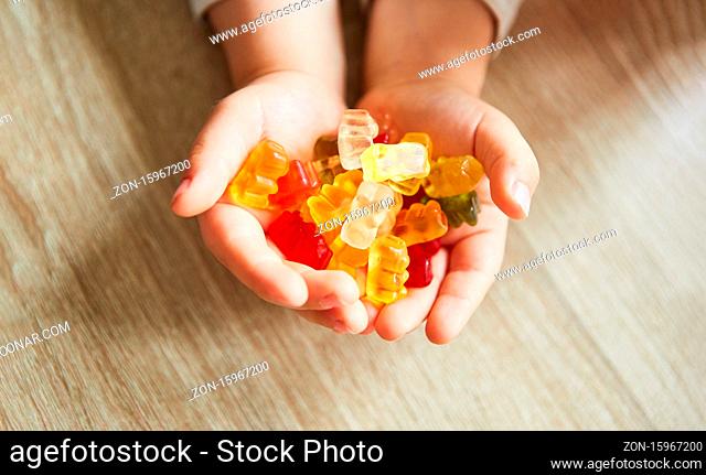 Hände von einem Kind halten bunte Gummibären als Süßigkeiten zum Naschen