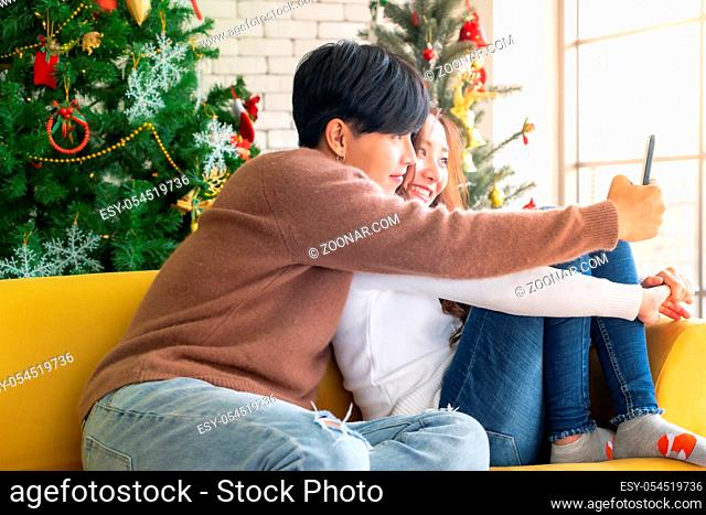 Young asian adult teenager coupletake selfie photographing for celebrateing christmas holiday together in living room with christmas tree decoration