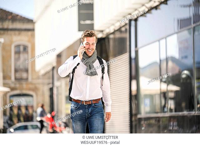 Smiling young man with backpack on the phone in the city