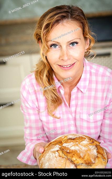 portrait of a woman in the kitchen who is holding fresh and fragrant bread in hands