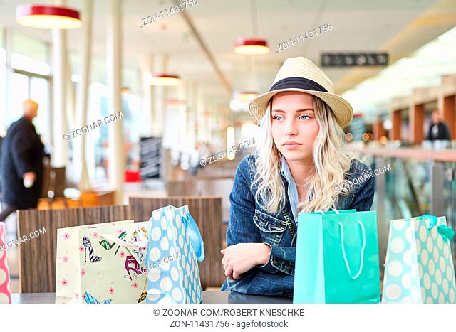 Blonde junge Frau sitzt nachdenklich mit vielen Tüten nach dem Shopping