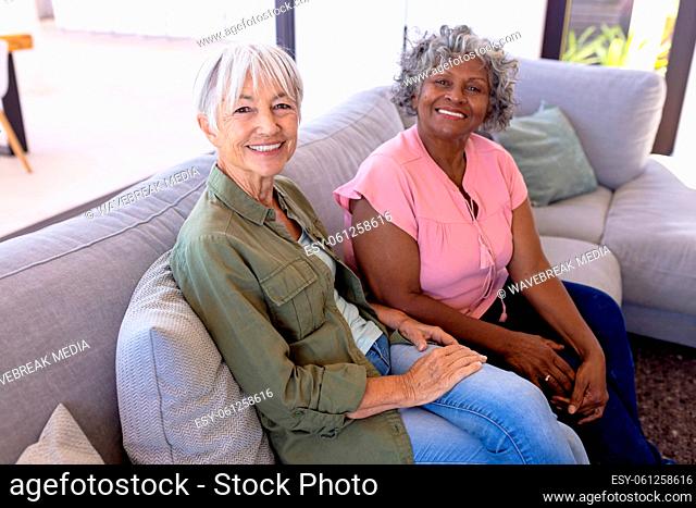 Portrait of smiling multiracial senior female friends sitting on sofa in living room at nursing home