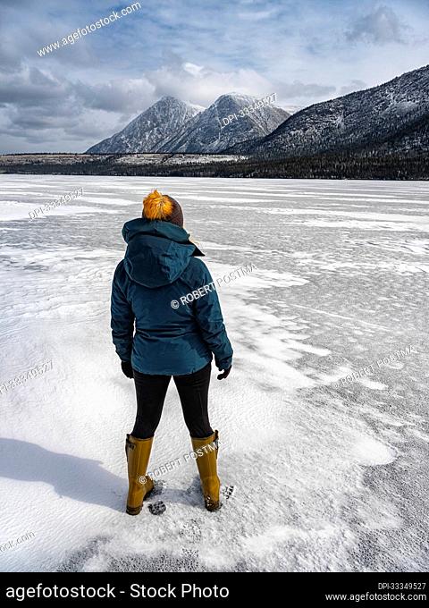 View taken from behind of a woman traveler standing on the frozen Kusawa Lake near Whitehorse; Yukon, Canada