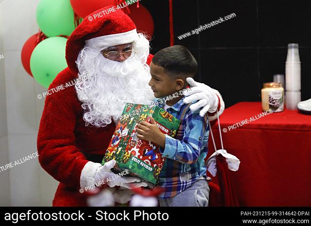 15 December 2023, Venezuela, Caracas: Children from the poor neighborhood of Petare receive presents from a man dressed as Santa Claus during the gift handover...