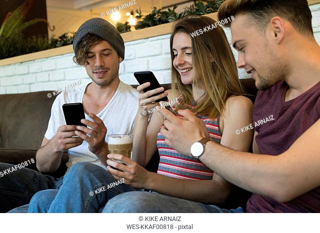 Three friends using their cell phones in a cafe