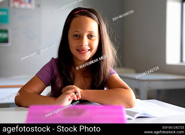 Portrait of smiling caucasian elementary schoolgirl sitting at desk in classroom