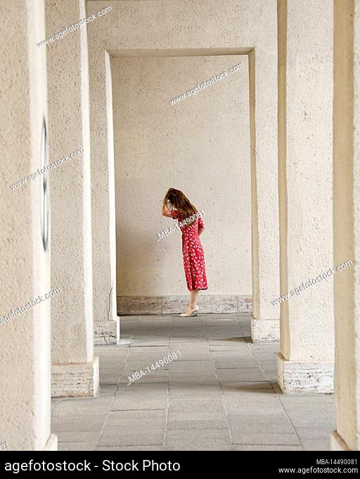 Woman in red dress, colonnade, standing, sideways, pensive