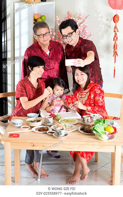 Happy Chinese New Year, taking selfie at reunion dinner. Happy Asian Chinese multi generation family with red cheongsam dining at home