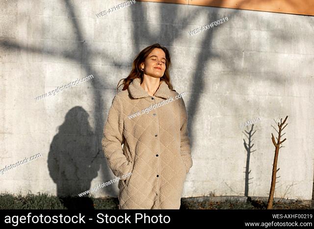 Beautiful woman with eyes closed standing in front of wall