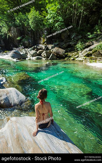 Woman wearing bikini sitting on rock by river