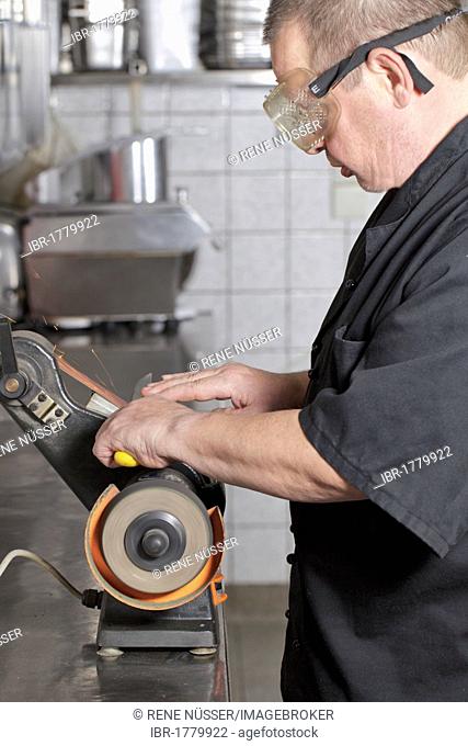 Chef sharpening a knife with a belt grinder in a kitchen