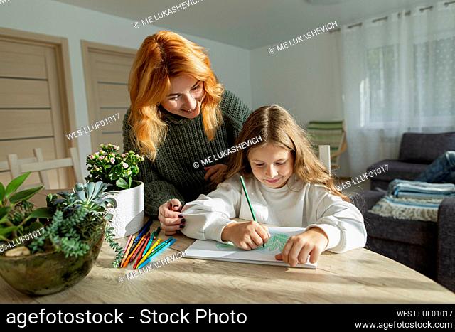 Girl drawing a picture at table watched by her mother