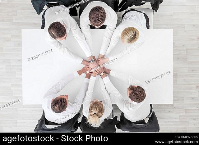 Business people team stacking hands sitting around white conference table in office unity cooperation concept