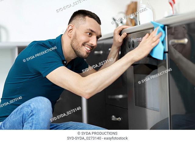 man with rag cleaning oven door at home kitchen