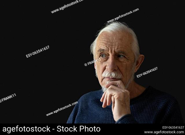 Beautiful gray hair old man wirh wrinkled face is posing on black background peeking to the right. Horizontally