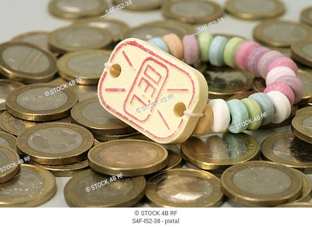 Wristwatch made of sweets lying on an accumulation of 1-Euro coins, close-up