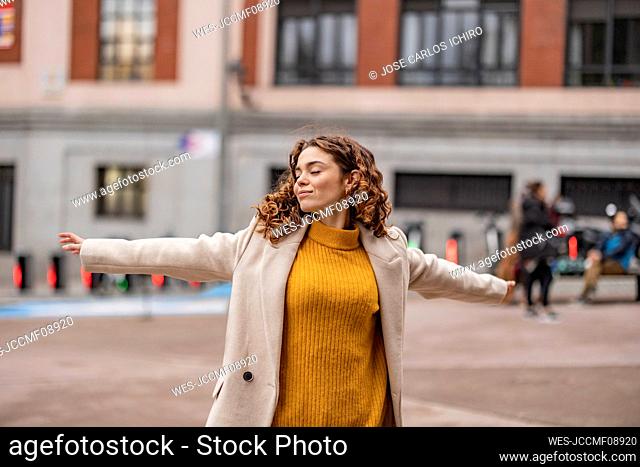 Smiling young woman with arms outstretched standing on footpath