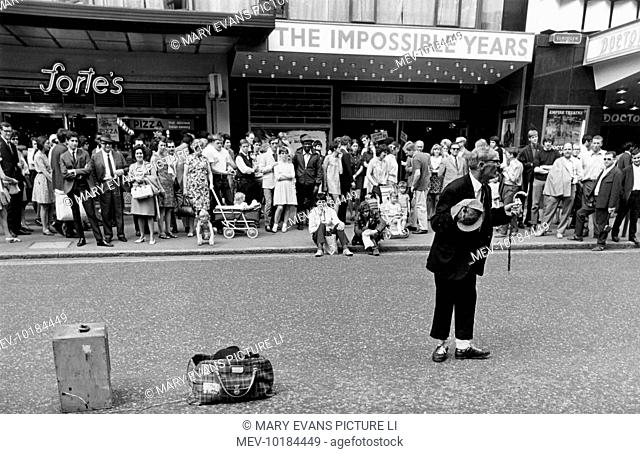 A street entertainer performs a trick involving a tartan bag and a wooden box, much to the amusement of the tourists in Leicester Square, London