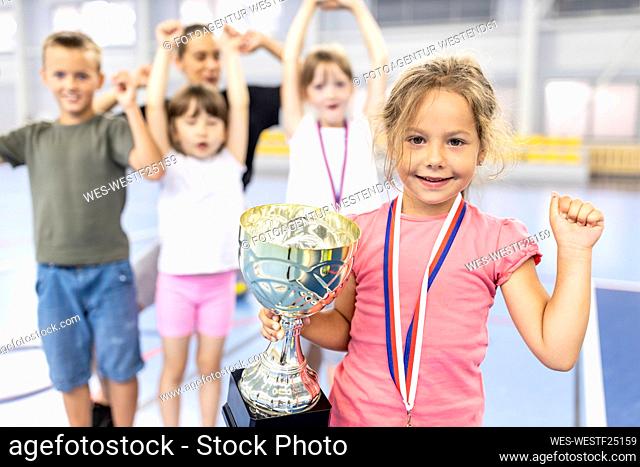 Girl with medal and trophy celebrating victory with friends at school sports court