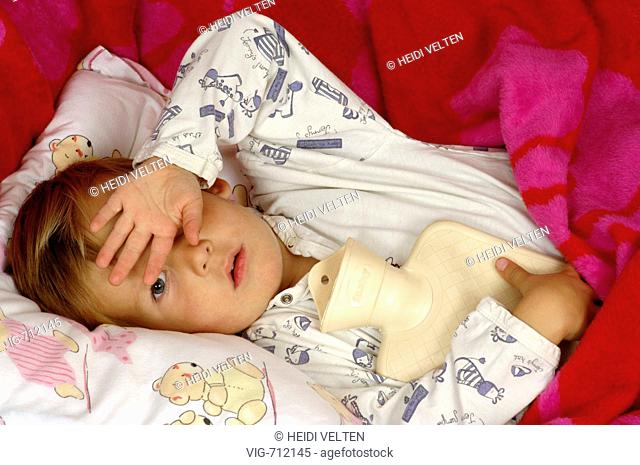 Little boy lies with hot-water bottle in bed. - GERMANY, 01/03/2008