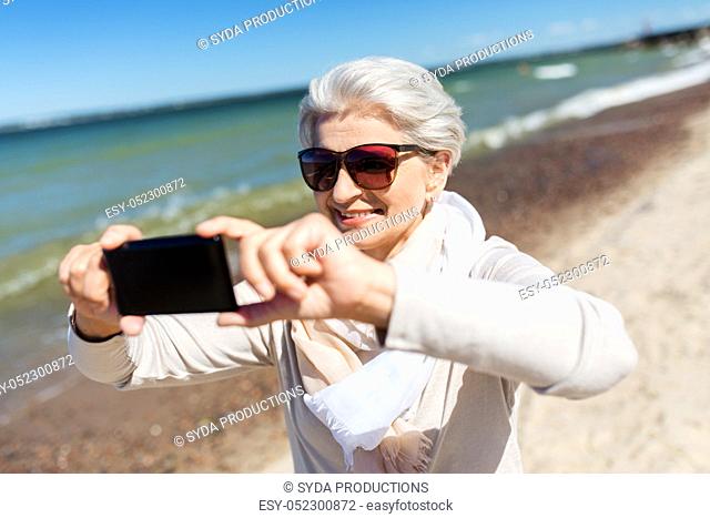 senior woman taking selfie by smartphone on beach
